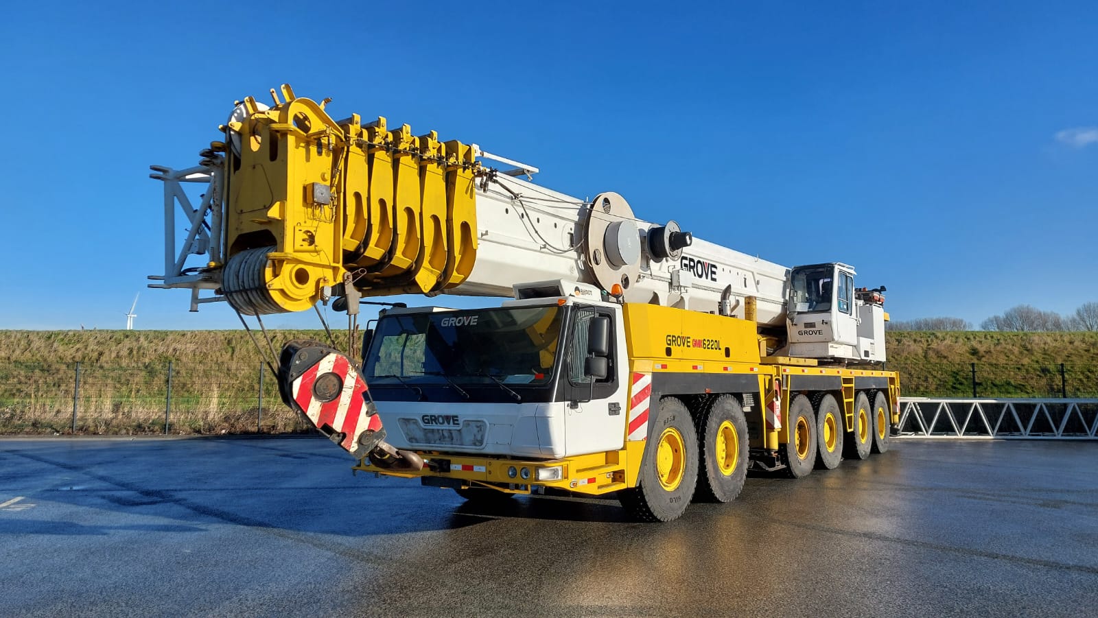 Used Grove GMK6220L all-terrain crane in yellow and white parked in a heavy equipment yard.