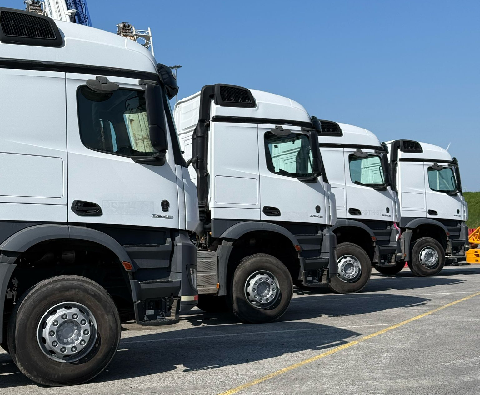 Four white used Mercedes-Benz 3348 6x4 trucks parked in a row at a heavy equipment yard.